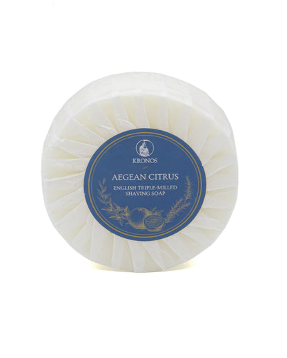 Kronos Aegean Citrus shaving soap, a round puck pleat-wrapped in white glassine paper with a navy and gold label, on a white background