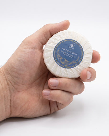 Kronos Aegean Citrus shaving soap held in a man's hand to show the size of the 65g puck