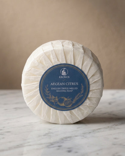 Kronos Aegean Citrus shaving soap standing on white marble against a warm beige wall