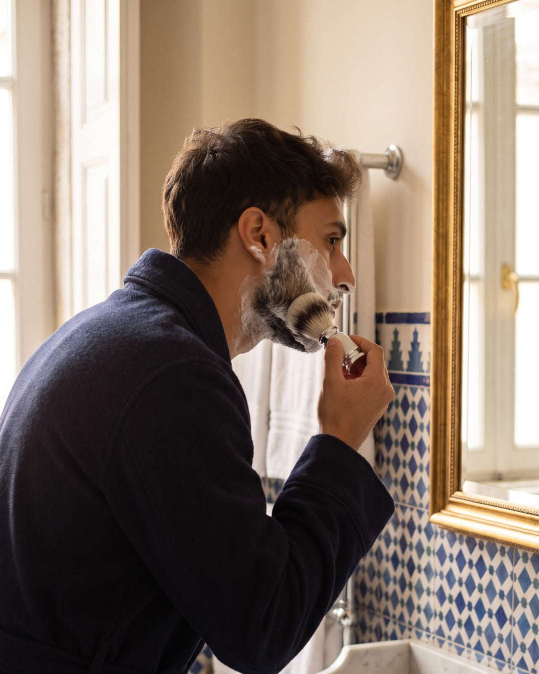 A man raising shaving lather with the Kronos shaving brush at a traditional bathroom basin