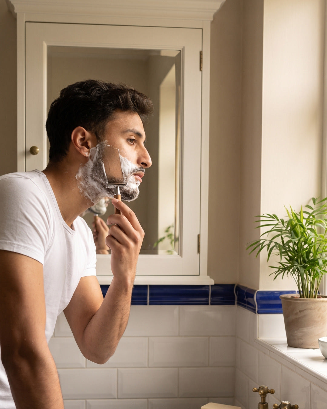 A man shaving with the Kronos bamboo safety razor in a heritage bathroom