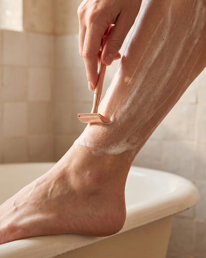 Shaving a leg with the rose gold razor at the edge of a bath