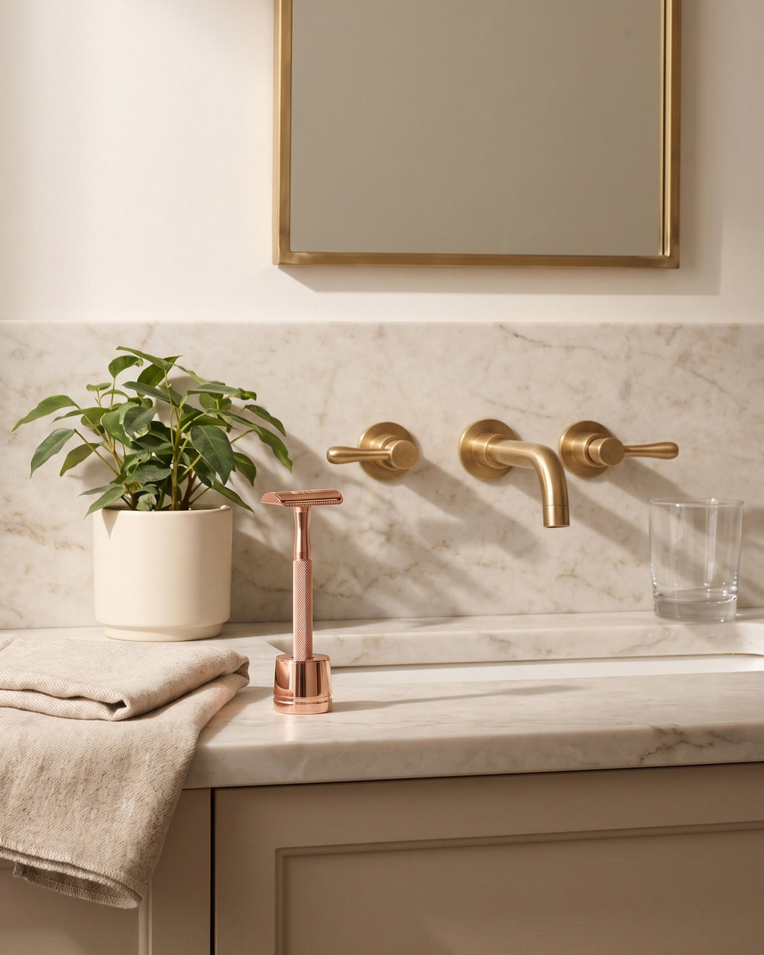 Rose gold razor on its stand on a marble vanity with brass taps