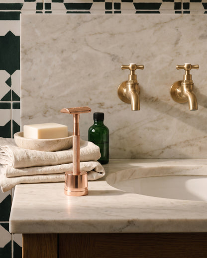 Rose gold razor on its stand beside folded towels and soap
