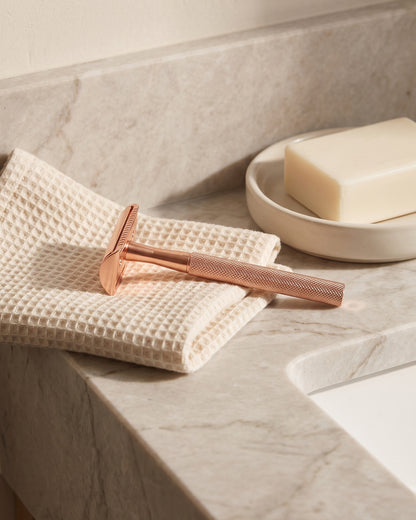 Rose gold razor resting on a waffle towel by a marble basin