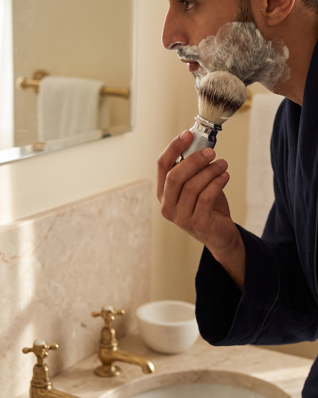 A man lathering with the Kronos shaving brush, the marble shaving bowl on the basin
